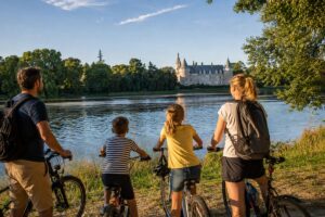 Une famille à vélo profite d’une balade au bord de la Loire, face à un château du Loiret